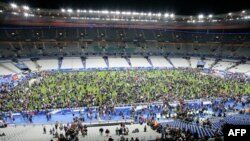 Людзі стаяць на полі стадыёну Stade de France пасьля выбухаў каля ўваходаў, 13 лістапада